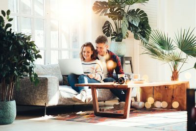 Young couple sitting on a sofa looking at mortgage holidays on their laptop