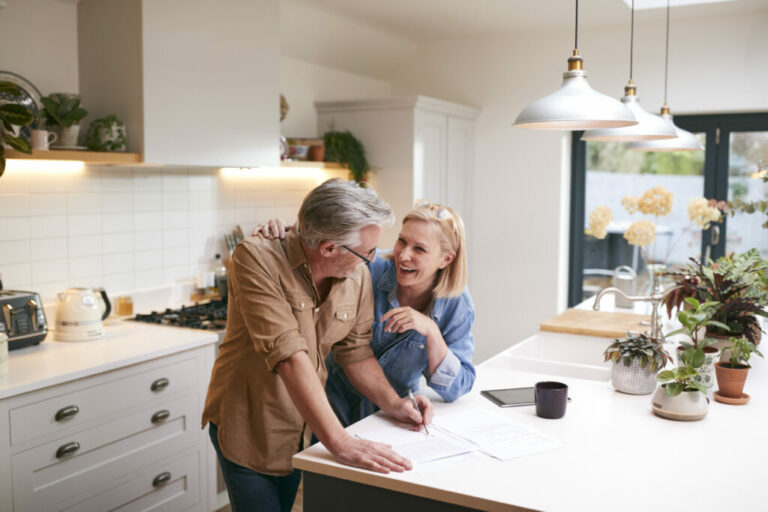 Mature couple at home in kitchen looking happy, working out their financial wellbeing