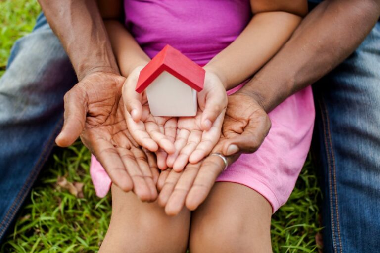 Child setting on parents lap, cupping a model house, investing through the ages